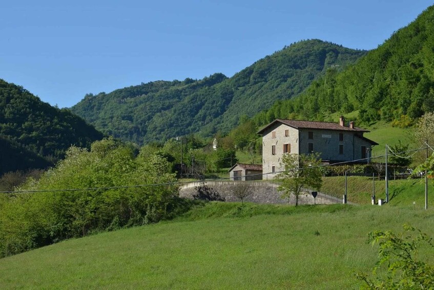 A stone house with a red roof in a lush green valley surrounded by forested hills. 2