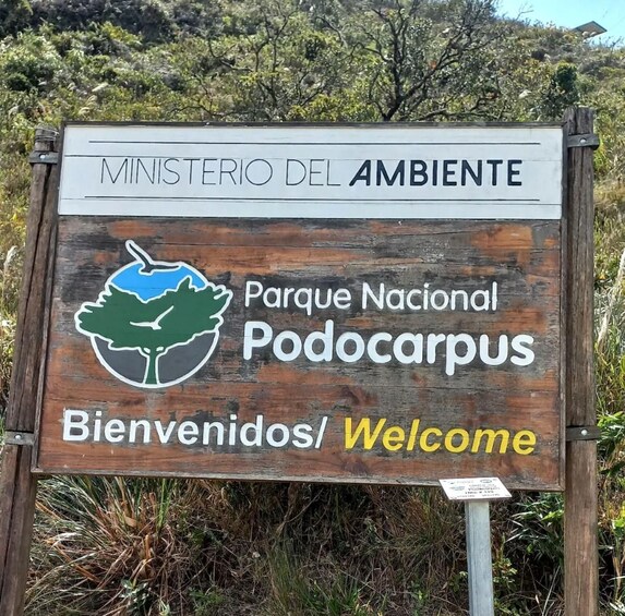 A welcome sign for Parque Nacional Podocarpus with a logo of a tree and a bird. 1