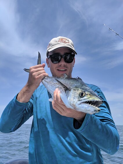 A person holding a fish with a fishing rod in the background. 3
