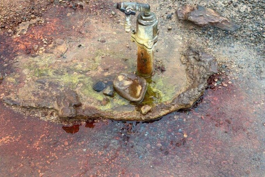 A rusty metal object, possibly a valve, on a wet, muddy surface with scattered rocks. 4