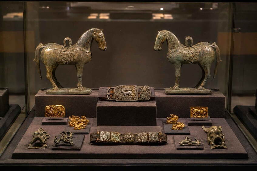 Une exposition d’objets anciens en bronze, comprenant deux statues de chevaux, une boucle de ceinture et diverses petites figurines. 5
