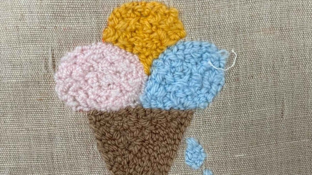 A crocheted ice cream cone with four scoops in yellow, pink, blue, and brown colors. 2