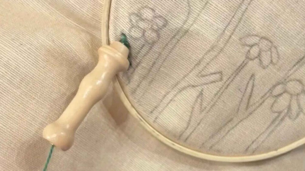 A close-up of a wooden embroidery hoop with a handle, a needle, and thread on a fabric background with floral embroidery. 4