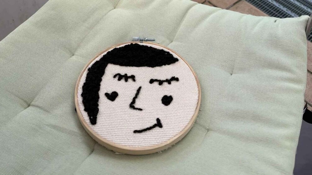 An embroidery hoop with a simple black and white face design on a light green cushion. 5