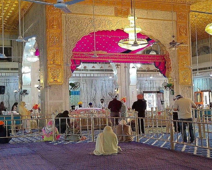 An ornate interior with a central archway, people seated and standing, and a patterned floor. 3