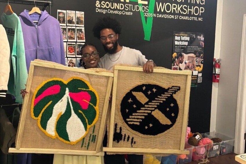 Two people holding framed artworks at a workshop. 5
