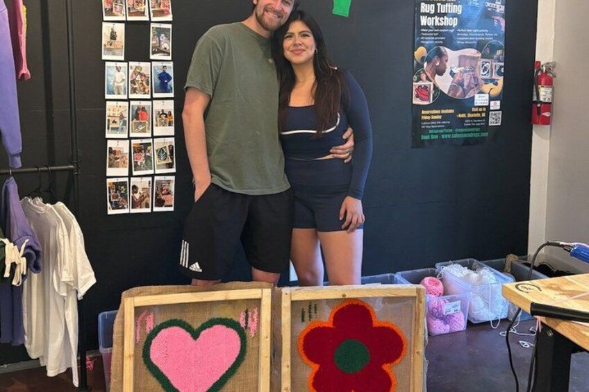 A man and woman standing in a room with a poster on the wall and a table with a heart and flower decoration. 4
