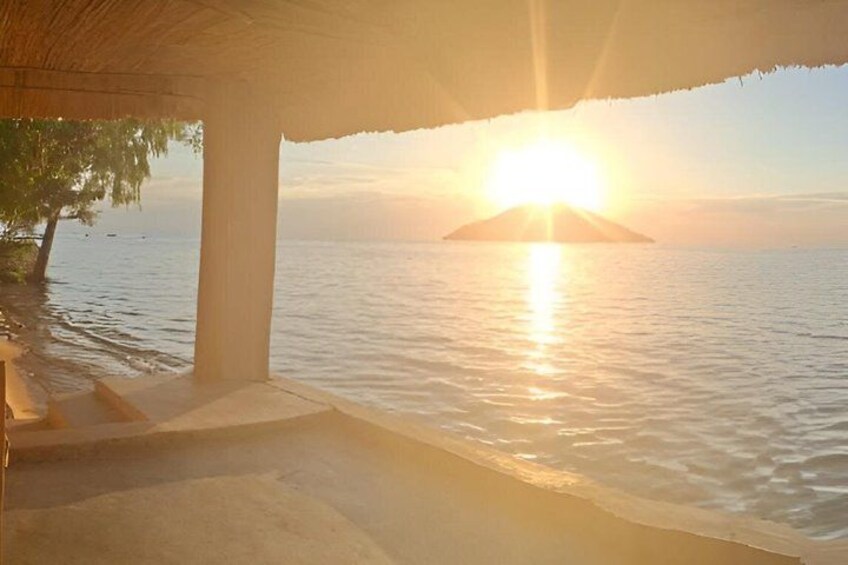 A sunset over water with a beach and a thatched roof structure. 3