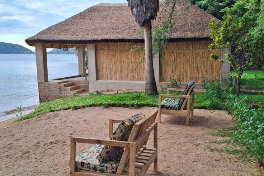 A beachside hut with a thatched roof, wooden chairs, and a sandy area. 4