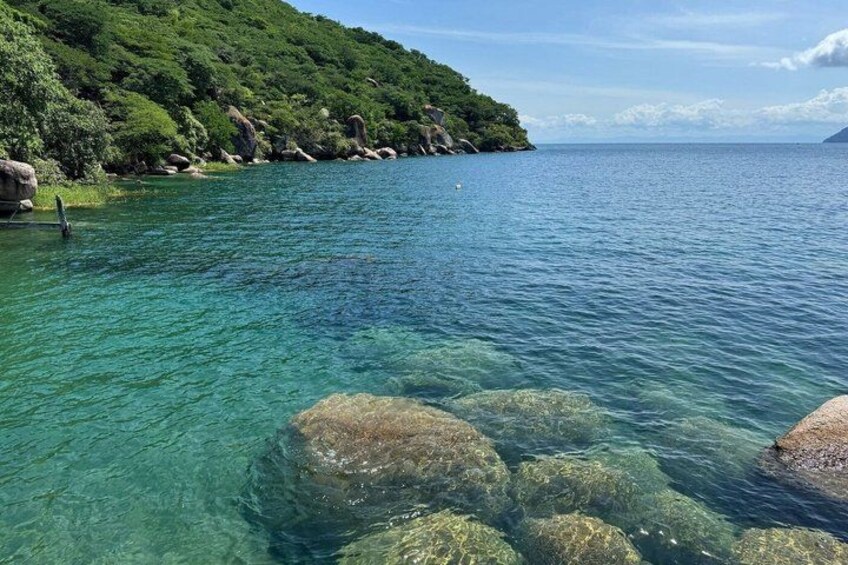 A clear coastal area with rocky outcrops and a lush green hillside. 5