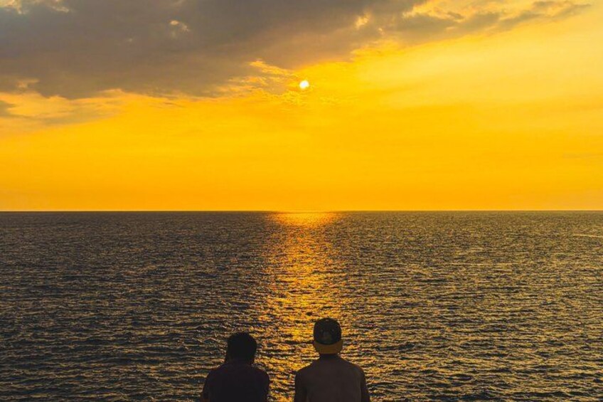 A sunset over the ocean with two silhouettes of people watching. 3