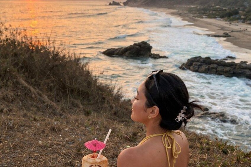 A person sitting on a cliff overlooking the ocean at sunset. 2