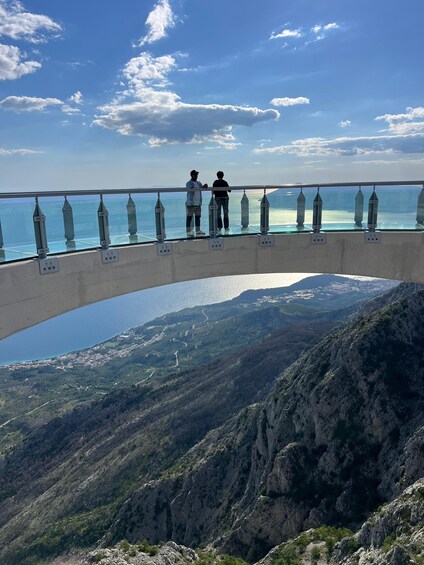 A bridge with a glass railing overlooking a valley and a body of water. 5