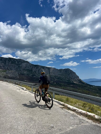 A cyclist on a paved road with a mountainous landscape in the background. 3