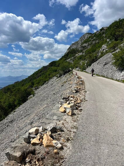 A paved road with a cyclist riding on a rocky hillside. 4