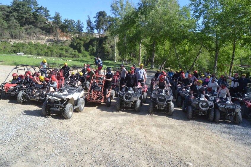 A group of people on ATVs lined up on a dirt road with trees and a grassy field in the background. 3