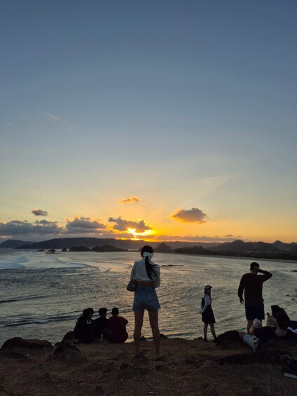 A sunset over a beach with people sitting and standing, watching the sky. 3