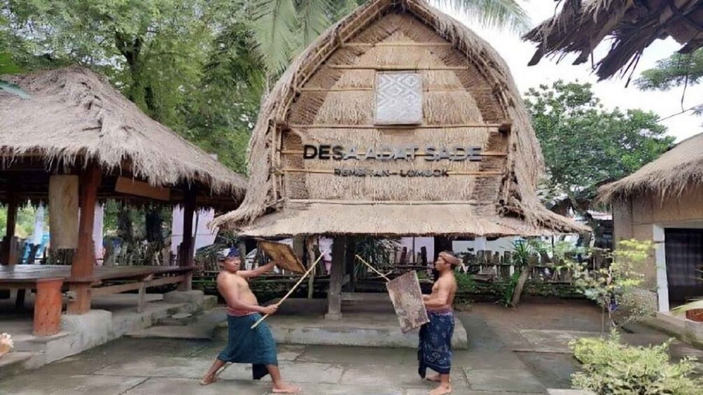 A traditional thatched-roof structure with inscriptions, surrounded by tropical vegetation and smaller huts. 4