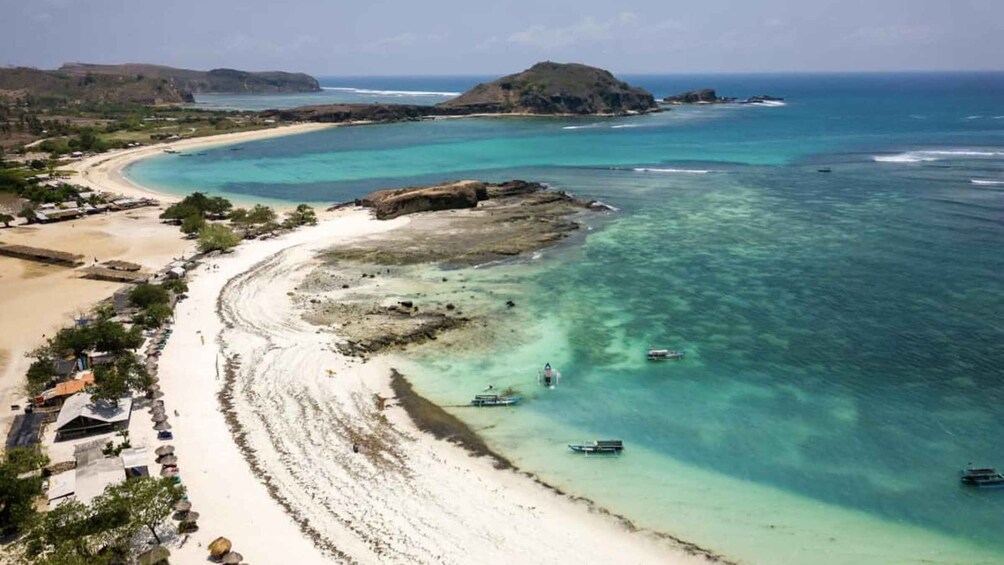 A coastal landscape with a sandy beach, clear turquoise waters, and a few boats. 2