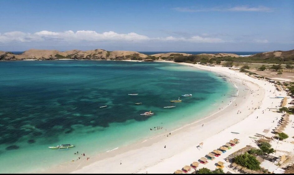 A beach with clear turquoise waters, boats, and umbrellas. 1