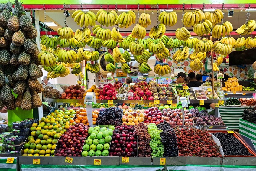 A fruit market with various fruits like bananas, pineapples, and grapes on display. 1