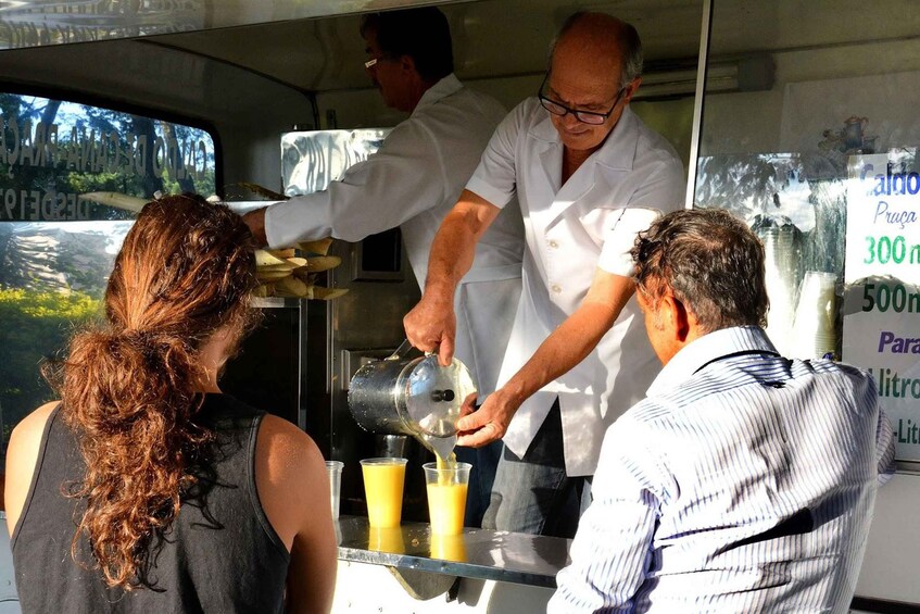 A person pouring a yellow liquid into a glass at a food stall. 4