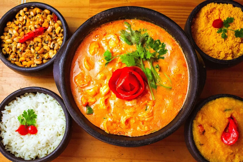 A bowl of curry with a red chili and cilantro garnish, surrounded by bowls of rice and other dishes. 2
