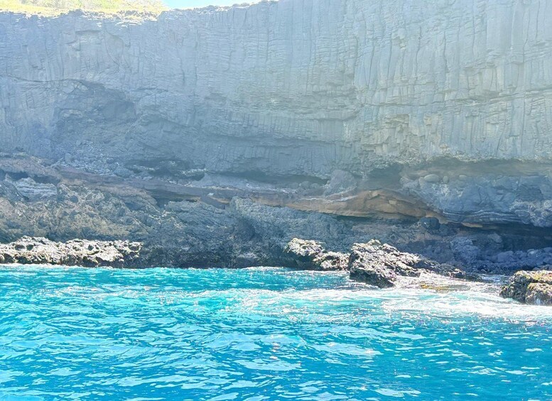A coastal cliff with clear blue water in the foreground. 2