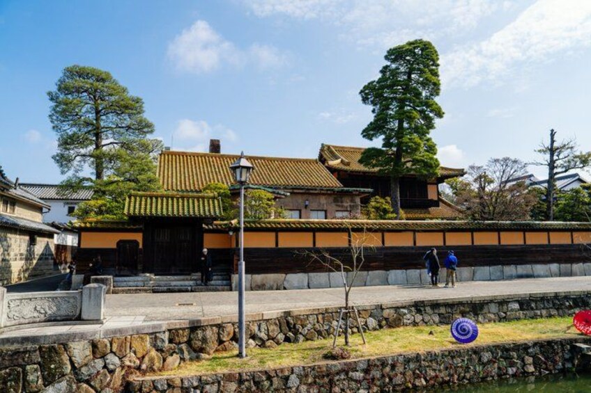 A traditional Japanese building with a tiled roof, stone wall, and a stone pathway leading to the entrance. 3