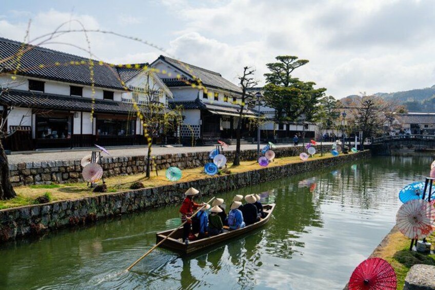 A traditional Japanese canal with a boat carrying passengers, surrounded by historic buildings and decorative umbrellas. 5