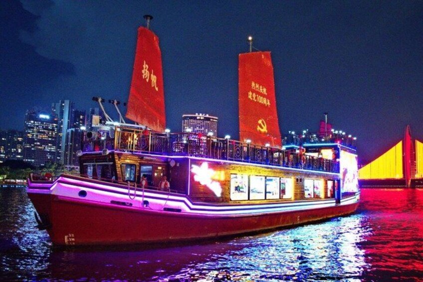 Ein hell beleuchtetes Boot mit roten Segeln und beleuchteten Fenstern liegt nachts an, mit einer Stadtlandschaft im Hintergrund. 2