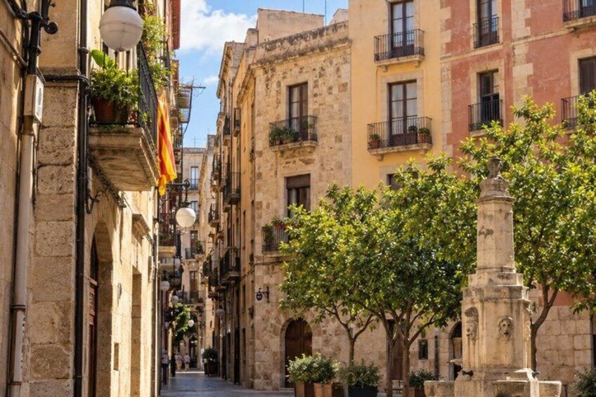 A narrow street lined with historic buildings, a statue, and trees. 2