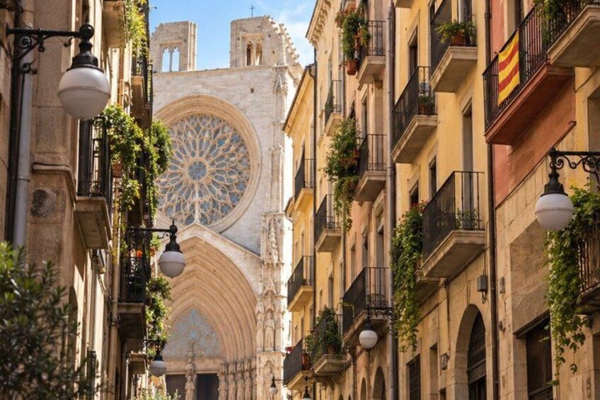 A narrow street with historic buildings, a large ornate window, and a bell tower. 5