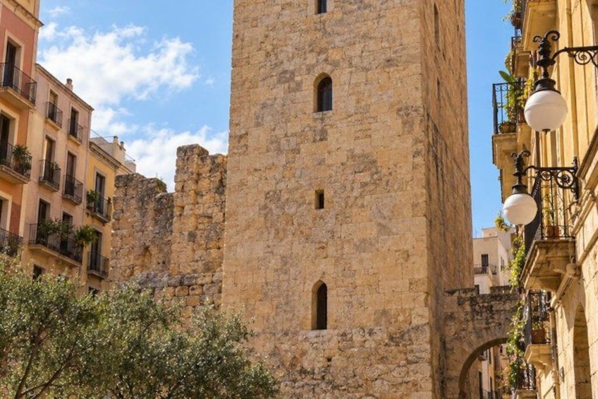 A historic stone tower with arched windows, surrounded by modern buildings with balconies and street lamps. 3