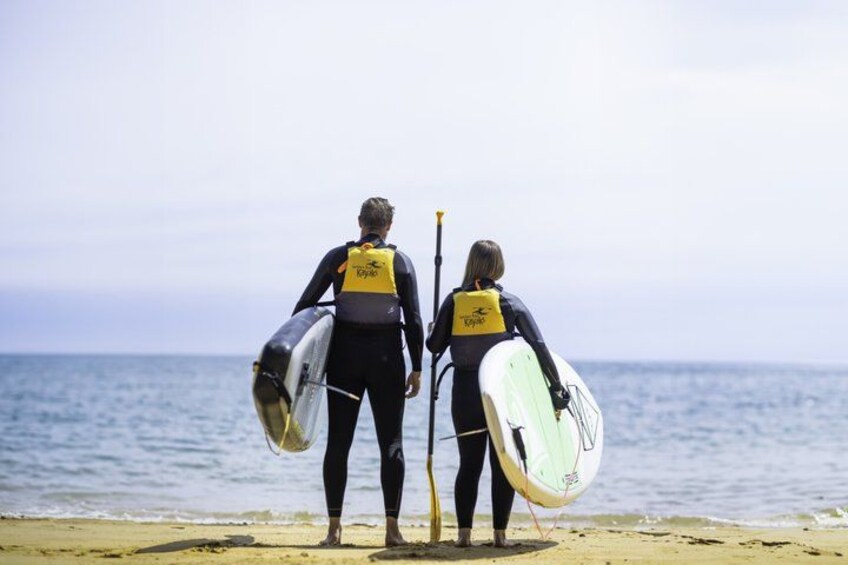 Two people in wetsuits carrying paddleboards on a beach. 5