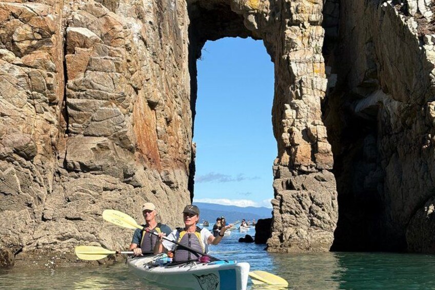 A group kayaking through a rocky arch formation. 3