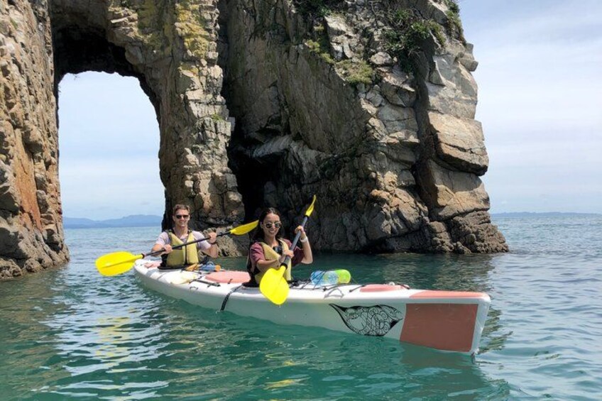 A kayak with two people paddling near a rocky arch formation. 4