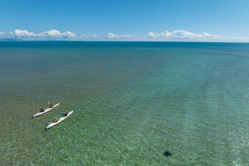 Two kayaks on a calm sea with clear water and distant land. 2