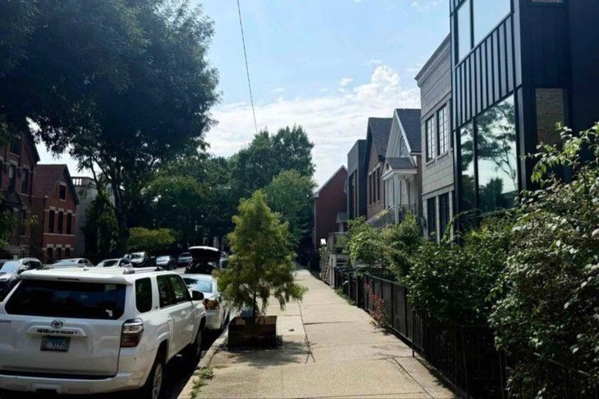 A residential street lined with parked cars, a sidewalk, and houses with large windows. 4