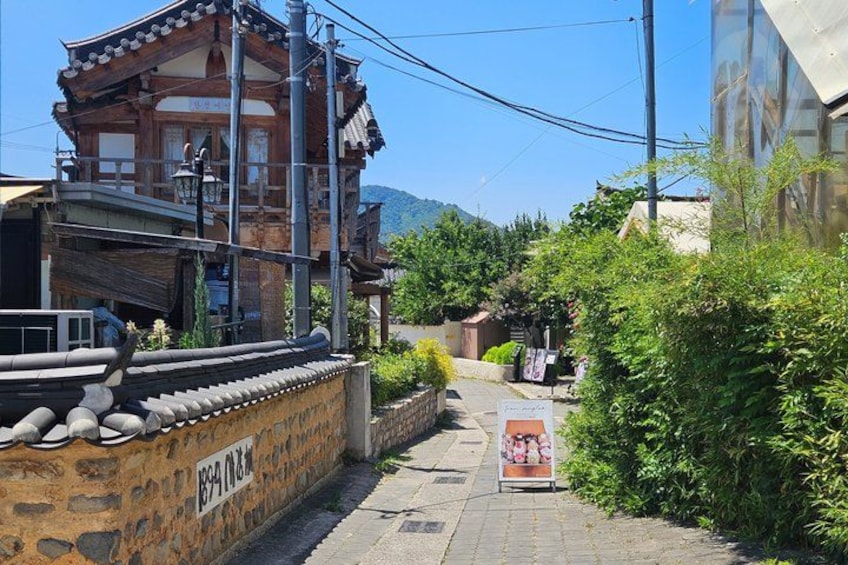 A traditional wooden building with a stone wall, a clear sky, and greenery. 1