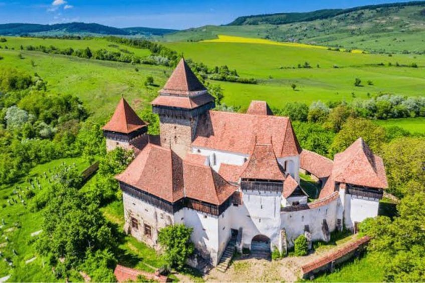 A castle with multiple towers surrounded by lush green fields and hills. 5