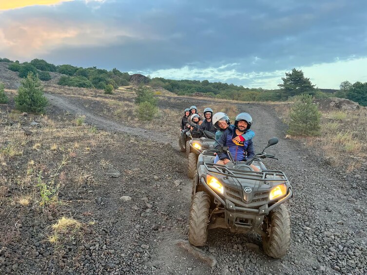 A group of people on an ATV on a dirt road with sparse vegetation and hills in the background. 1
