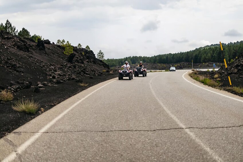 A paved road with two people riding ATVs and a car in the distance. 3