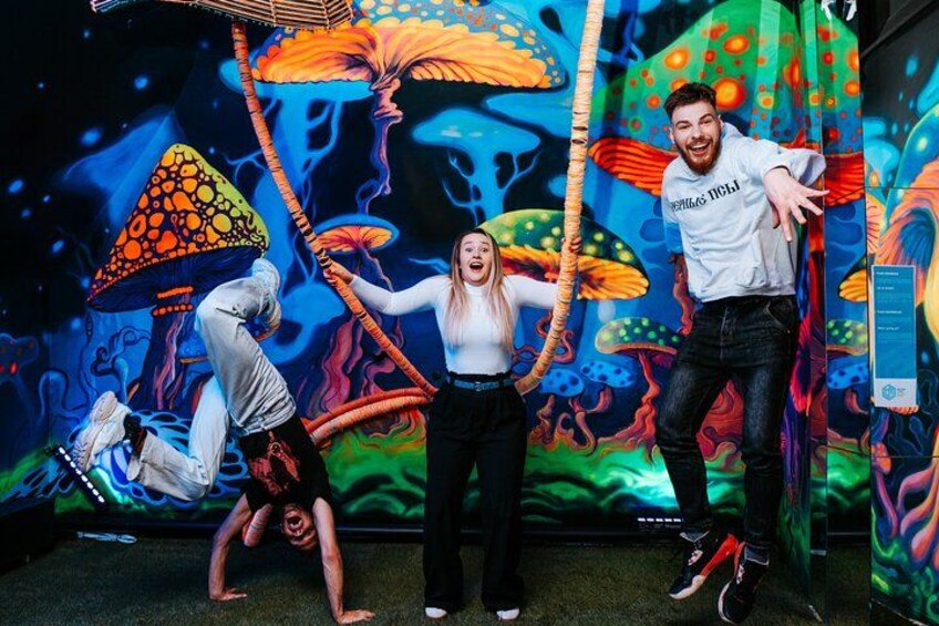 Three people performing acrobatics in front of a colorful mural with mushrooms and abstract designs. 2
