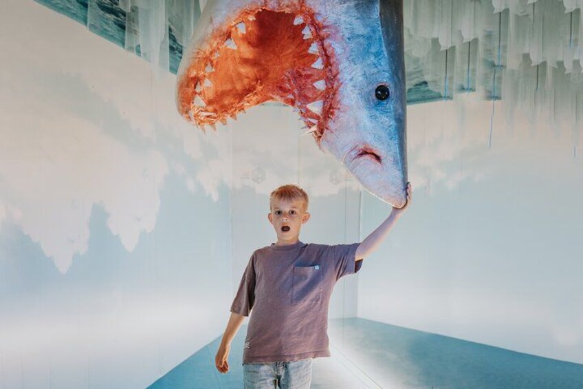 A person holding a large shark model in a museum. 4