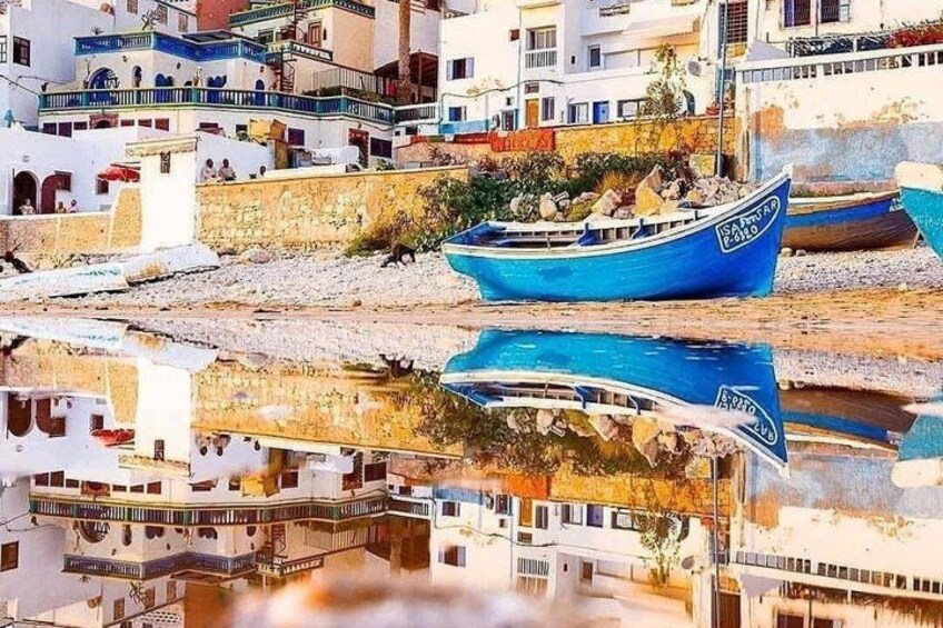 A coastal village with traditional white buildings, a blue boat with 'SANTURNO' written on it, and its reflection in the water. 4