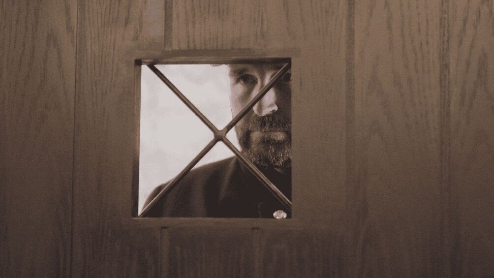 A person peering through a window with a wooden frame. 4