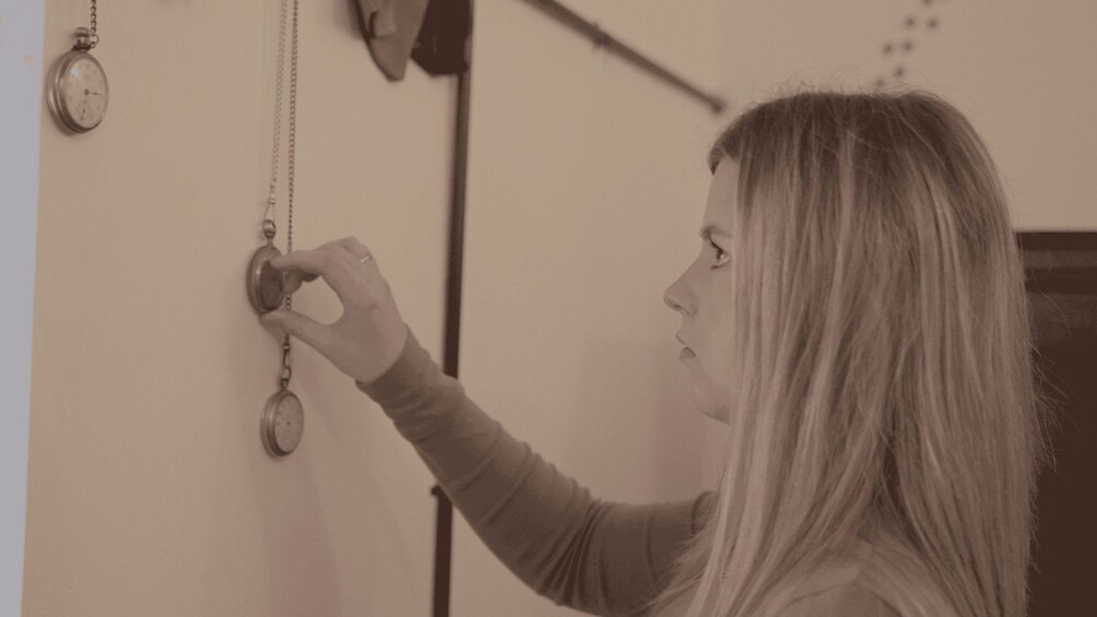 A person adjusting a wall-mounted pocket watch. 2