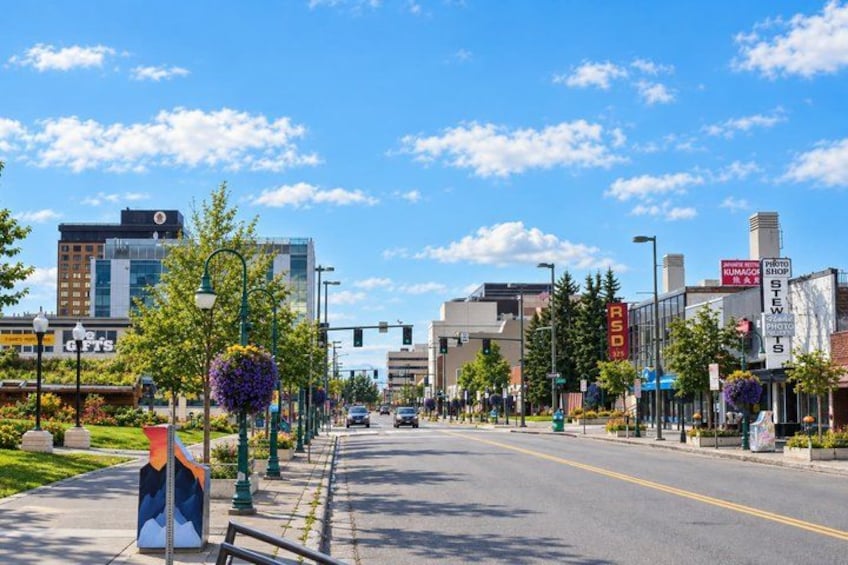 A city street with buildings, trees, and a clear sky. 1