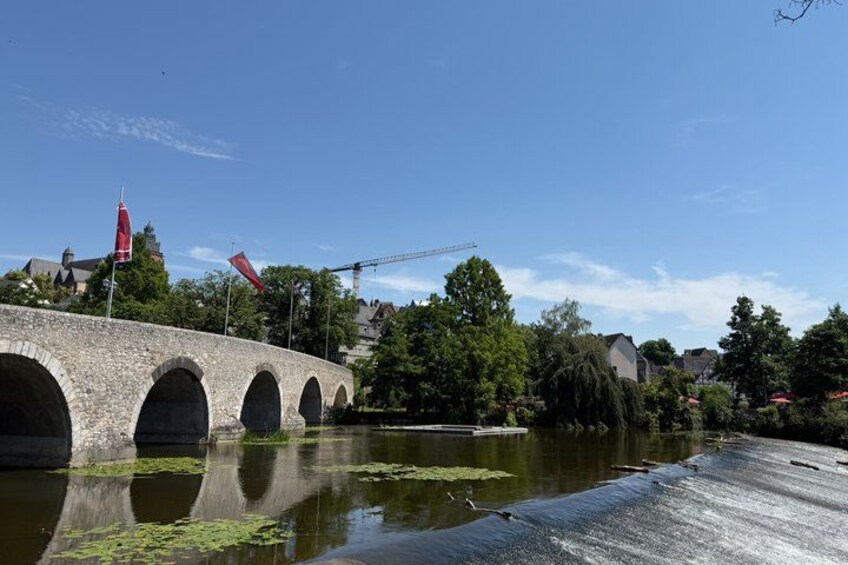 A stone bridge over a river with greenery and buildings in the background. 5